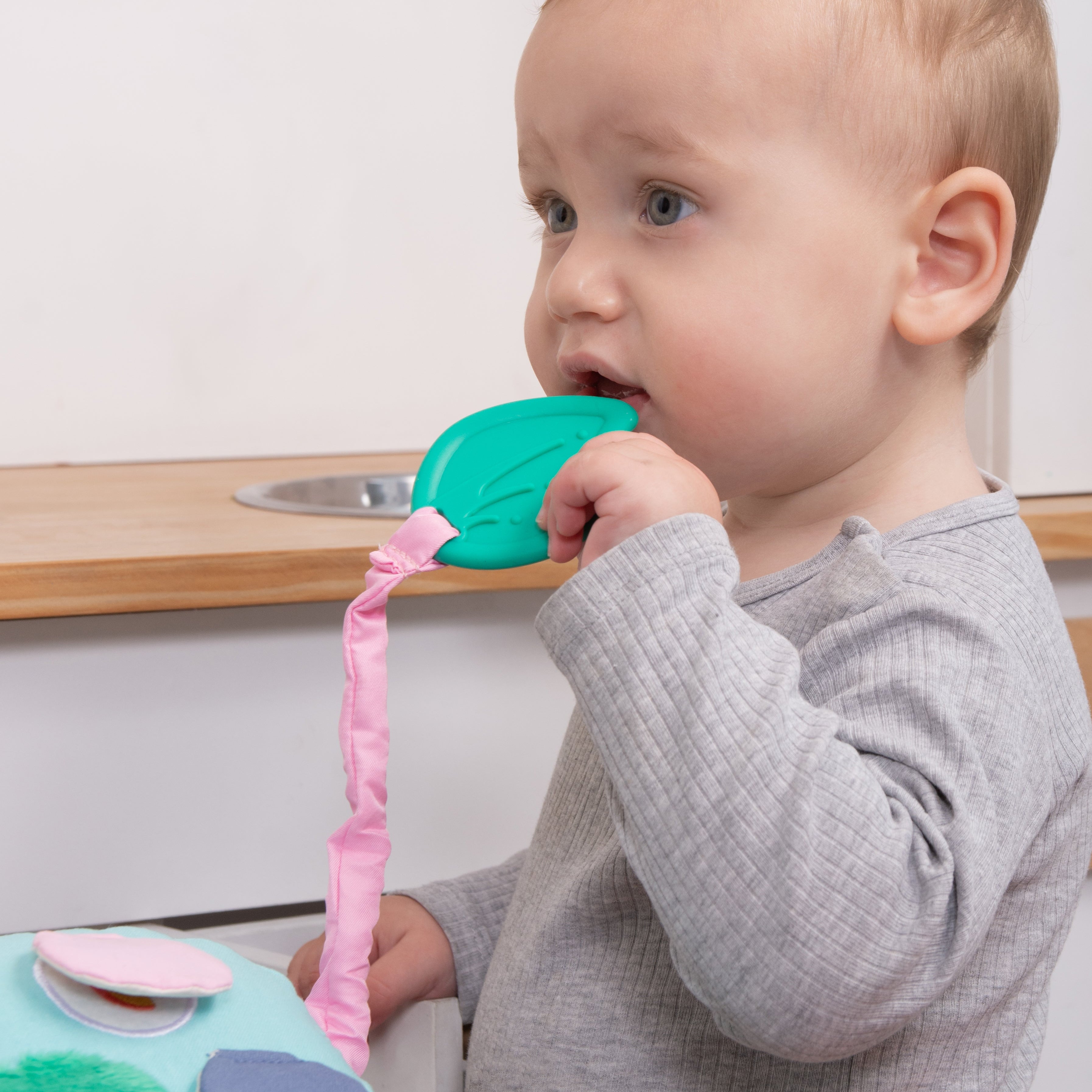 A baby in a gray long-sleeve shirt holds Birdsong's elephant's teether tail 