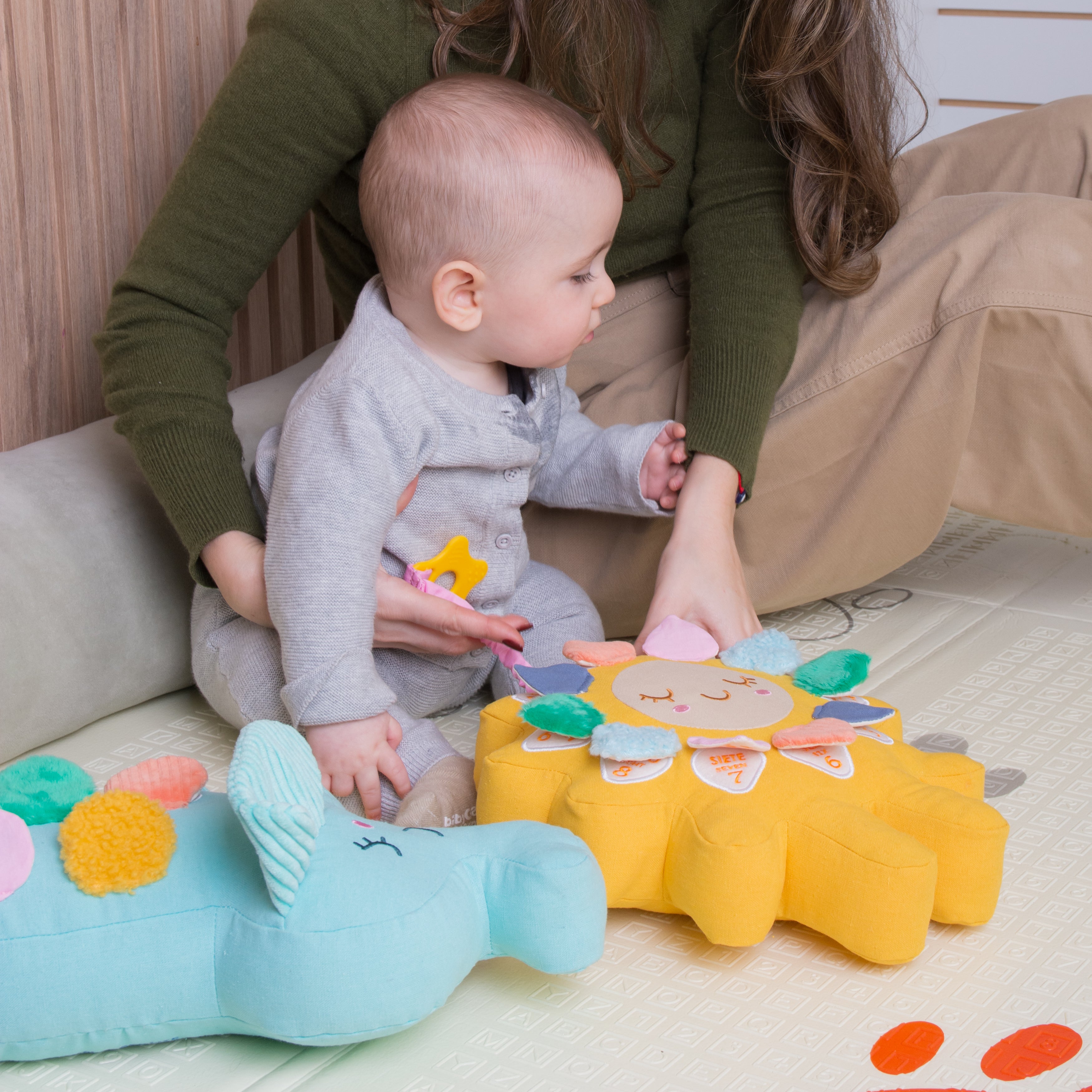 A baby is seating next to his mom while he plays with Birdsongs' two toys.
