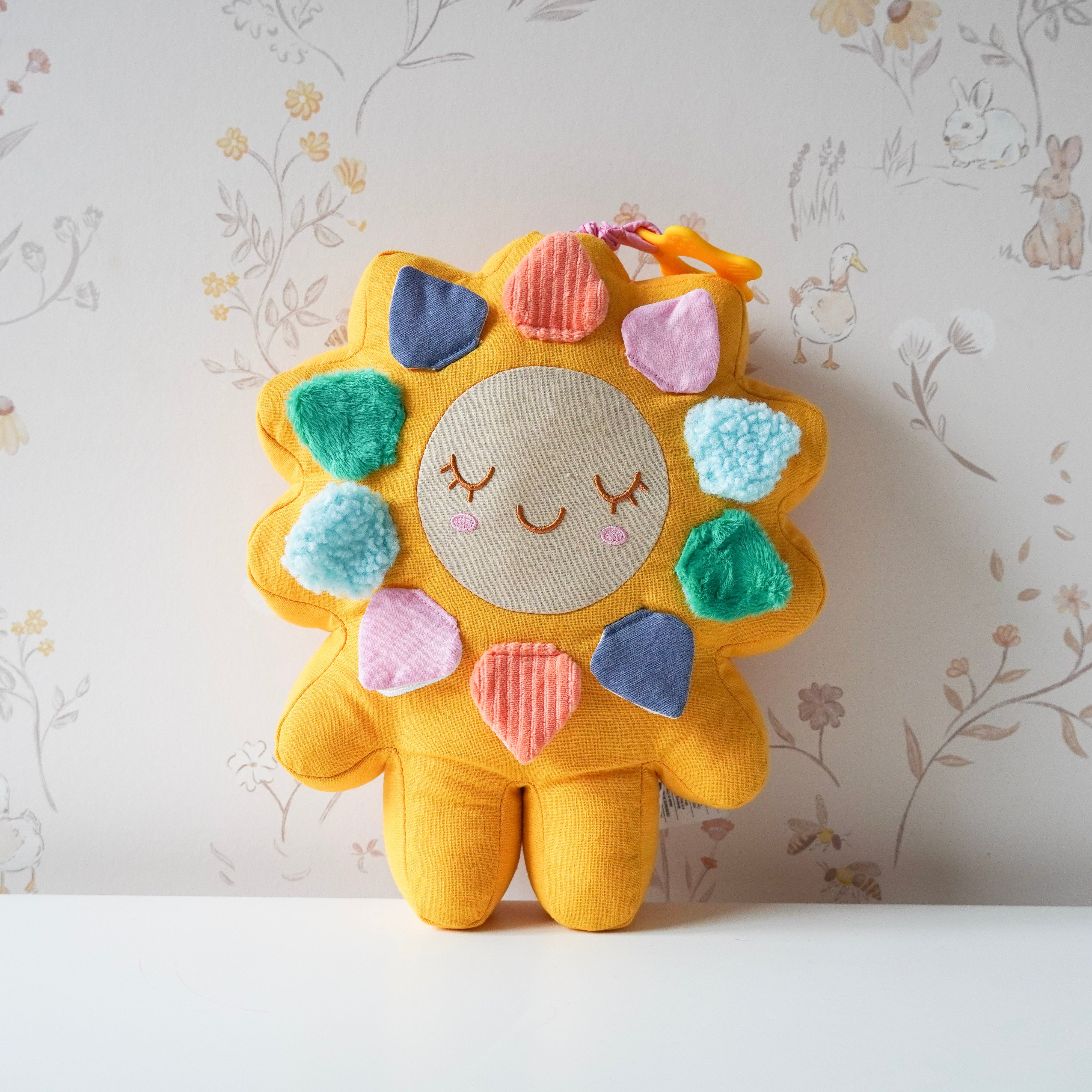 Sun-shaped plush toy with colorful flaps on a floral-patterned wall background