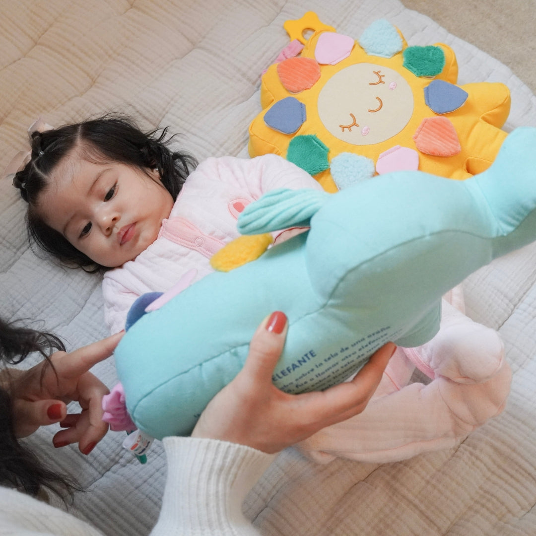 Baby lying on the floor looking at Birdsong's bilingual elephant toy while her mom points to one of the flaps from the elephant
