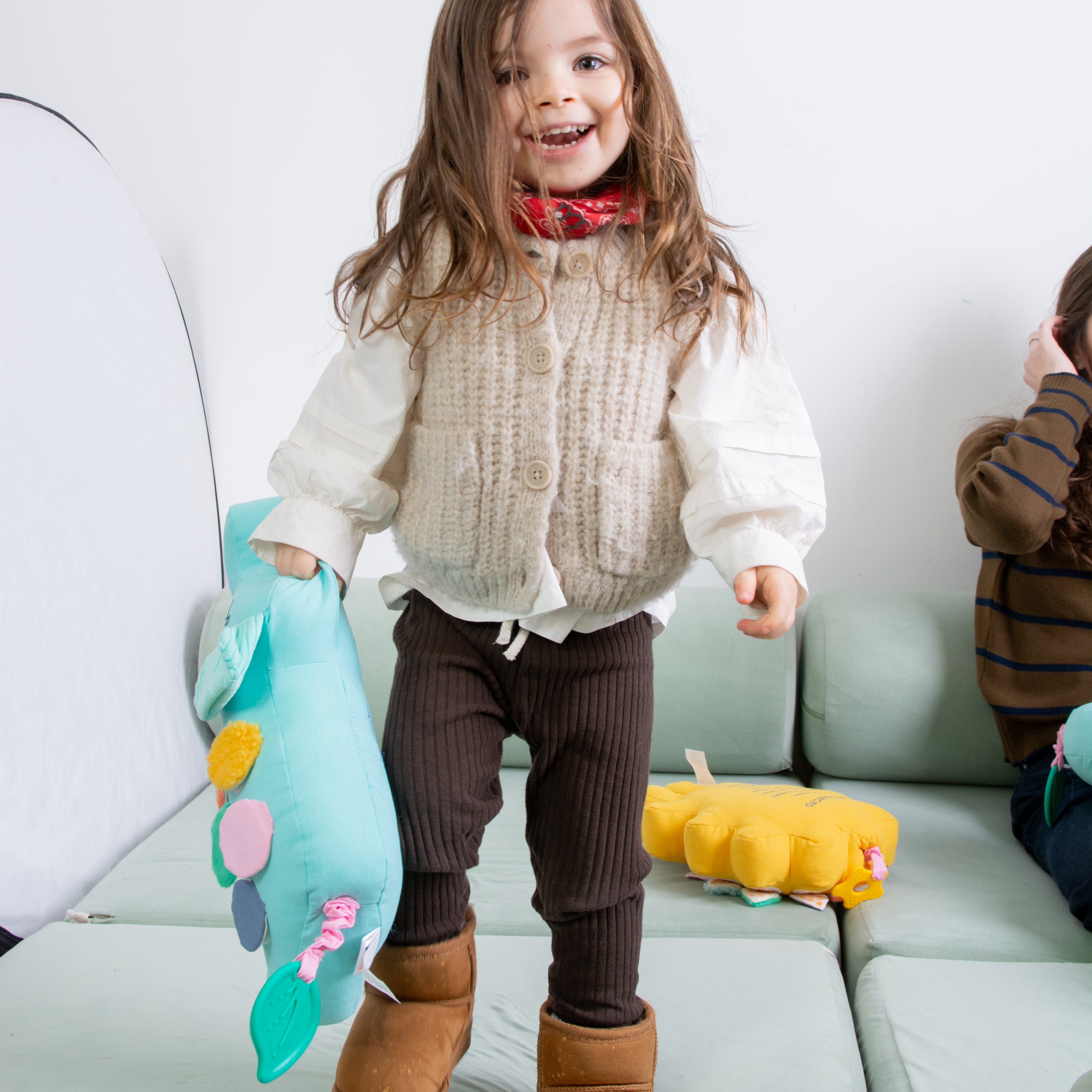 A toddler girl is holding Birdsong's bilingual elephant toy and smiling of happiness. 